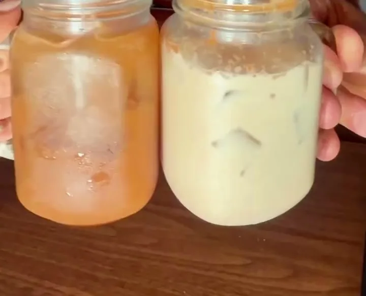 Two mason jars of aguas frescas, horchata and tamarindo, held up in the dining room at Autentica Taqueria